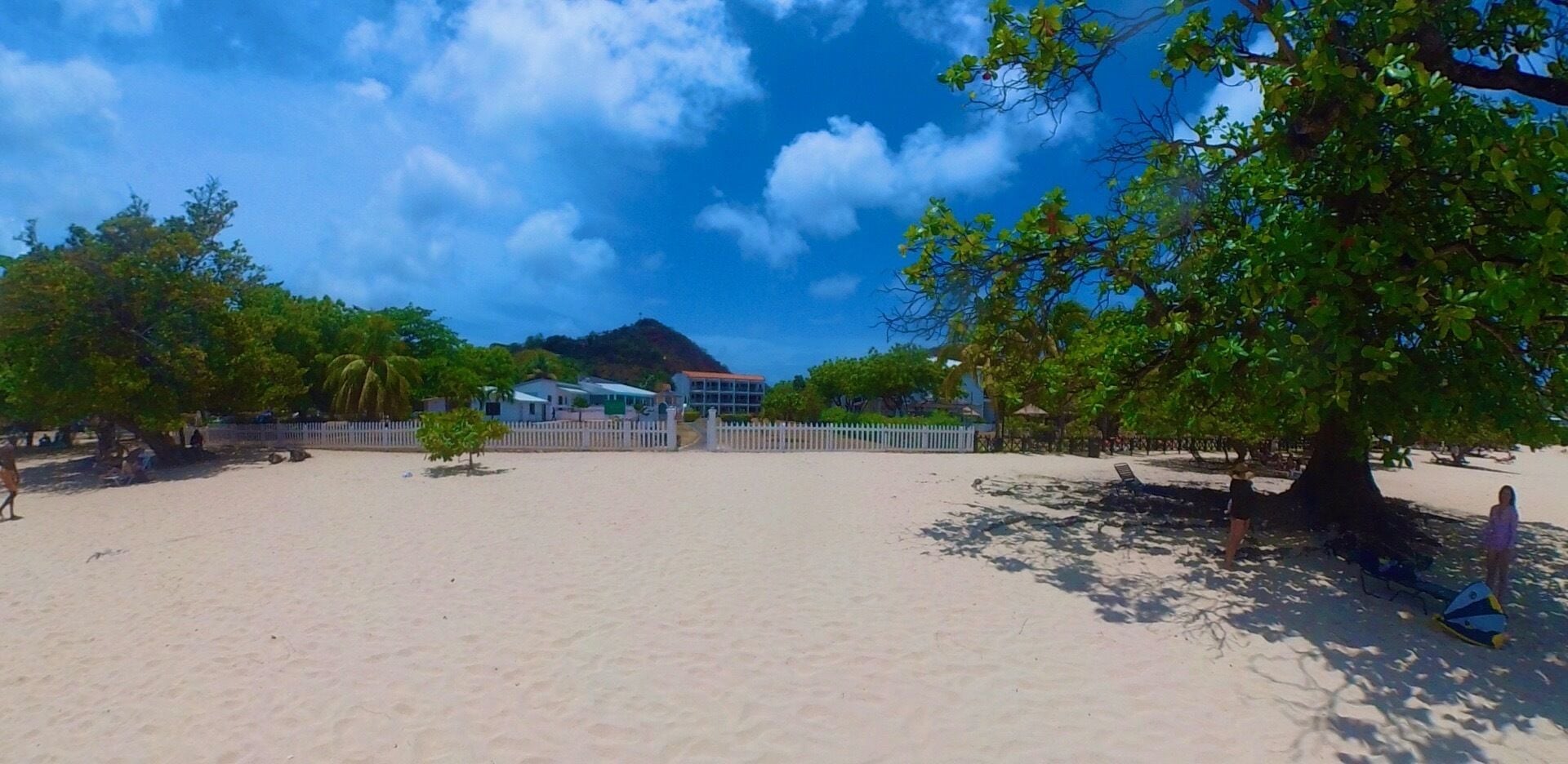 A beach with a white fence, trees, and buildings in the background.