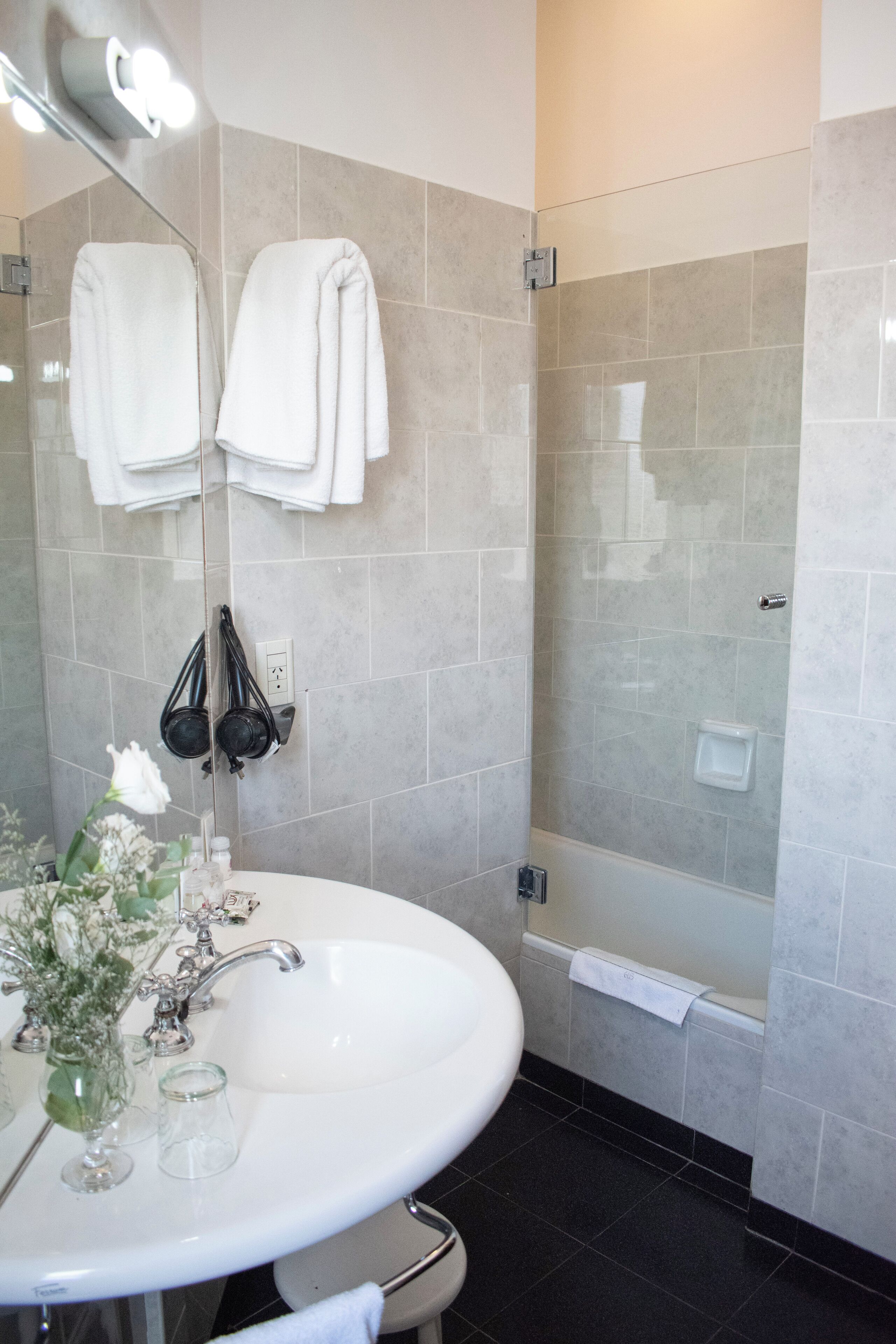 A bathroom with a white sink, a mirror, a towel rack with towels, a glass shower enclosure, and a bathtub.