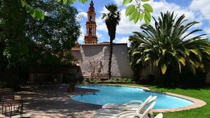 A swimming pool with lounge chairs, a palm tree, and a building with a bell tower.