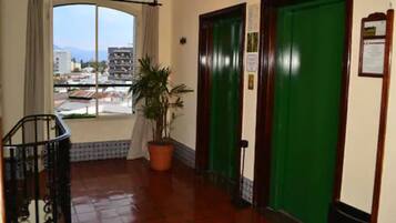 Un vestíbulo de hotel con un ventanal grande, una planta en maceta, una escalera y dos puertas verdes.