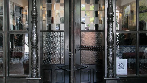 A hotel entrance with ornate ironwork, a date plaque, and a QR code.