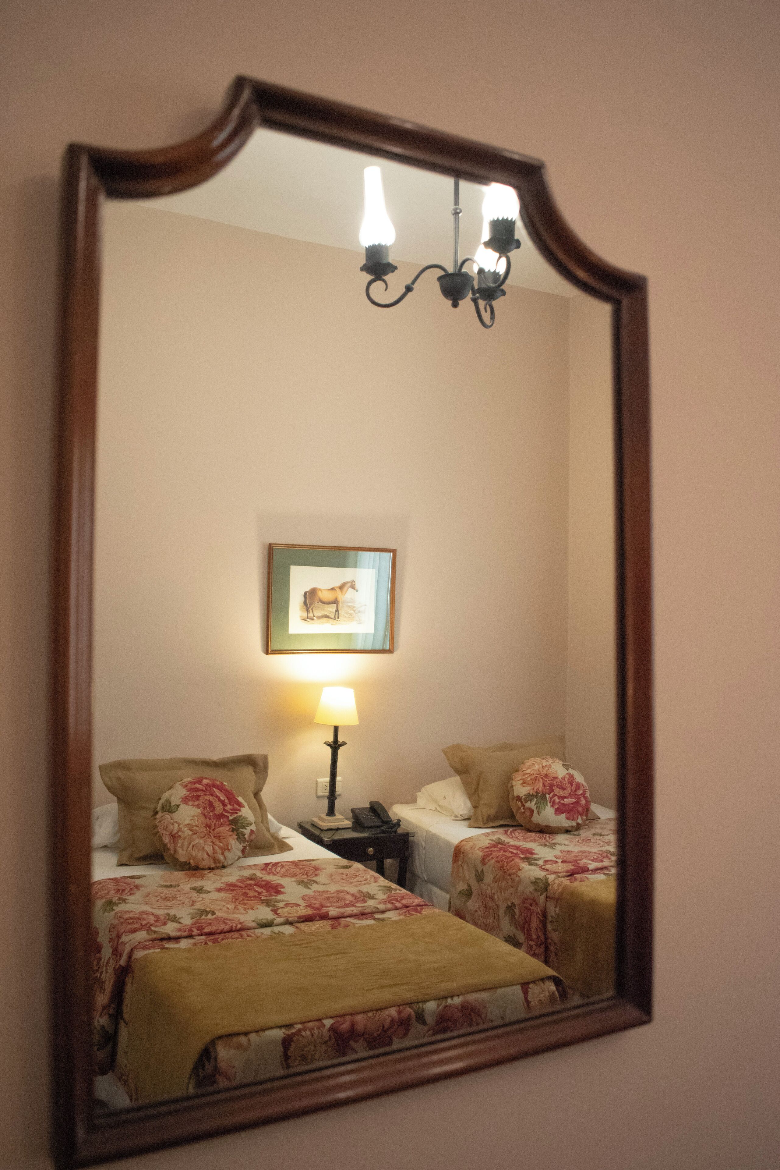 Une chambre avec deux lits, une table de chevet, une lampe, un tableau encadré au mur et un lustre.