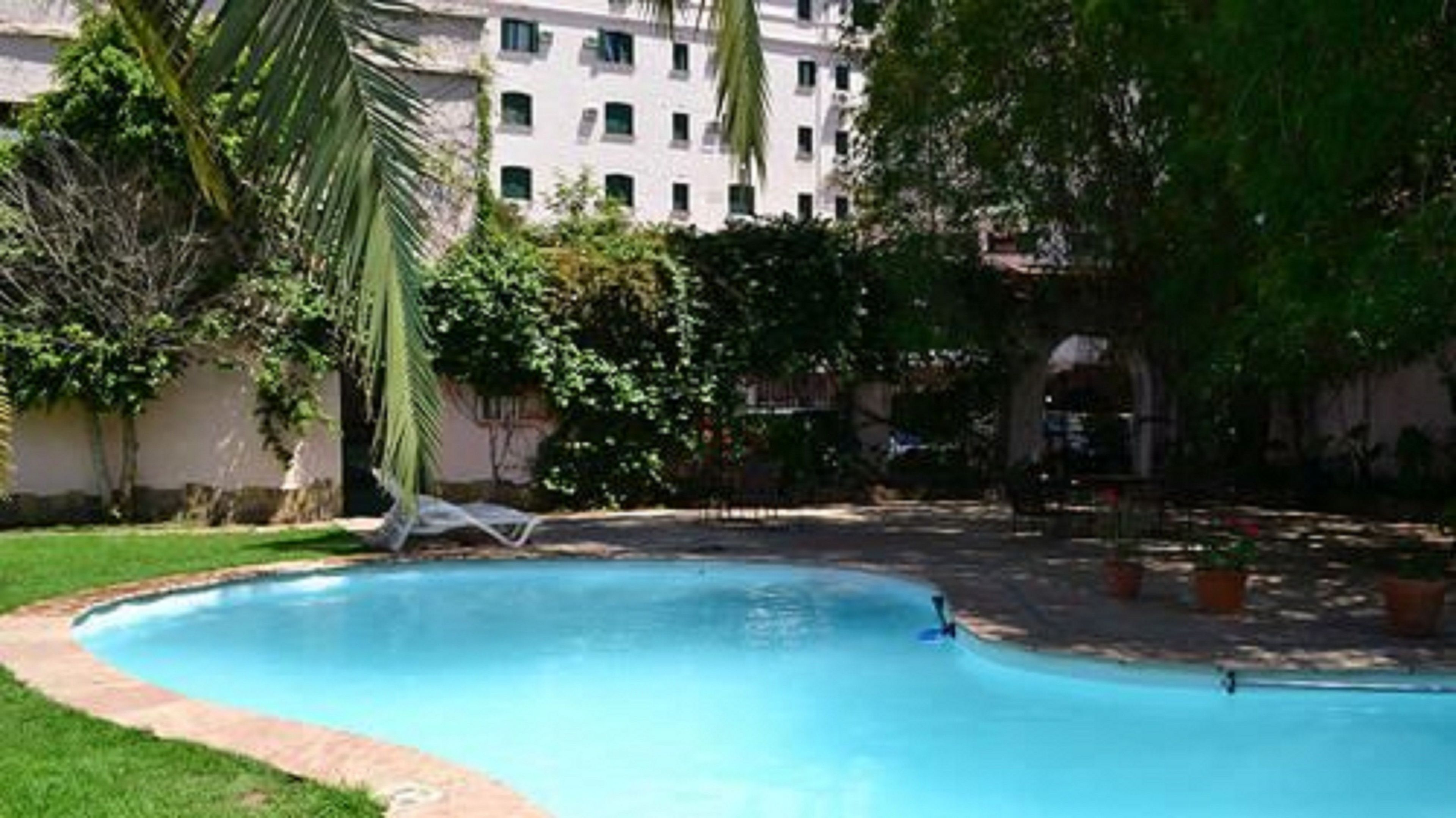 Piscina rodeada por vegetação e um edifício ao fundo.