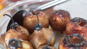 A glass dish containing glazed pears with a caramelized top, placed on a wooden table.