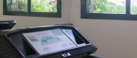 Una caminadora con pantalla digital, ubicada junto a una ventana con vista a espacios verdes.
