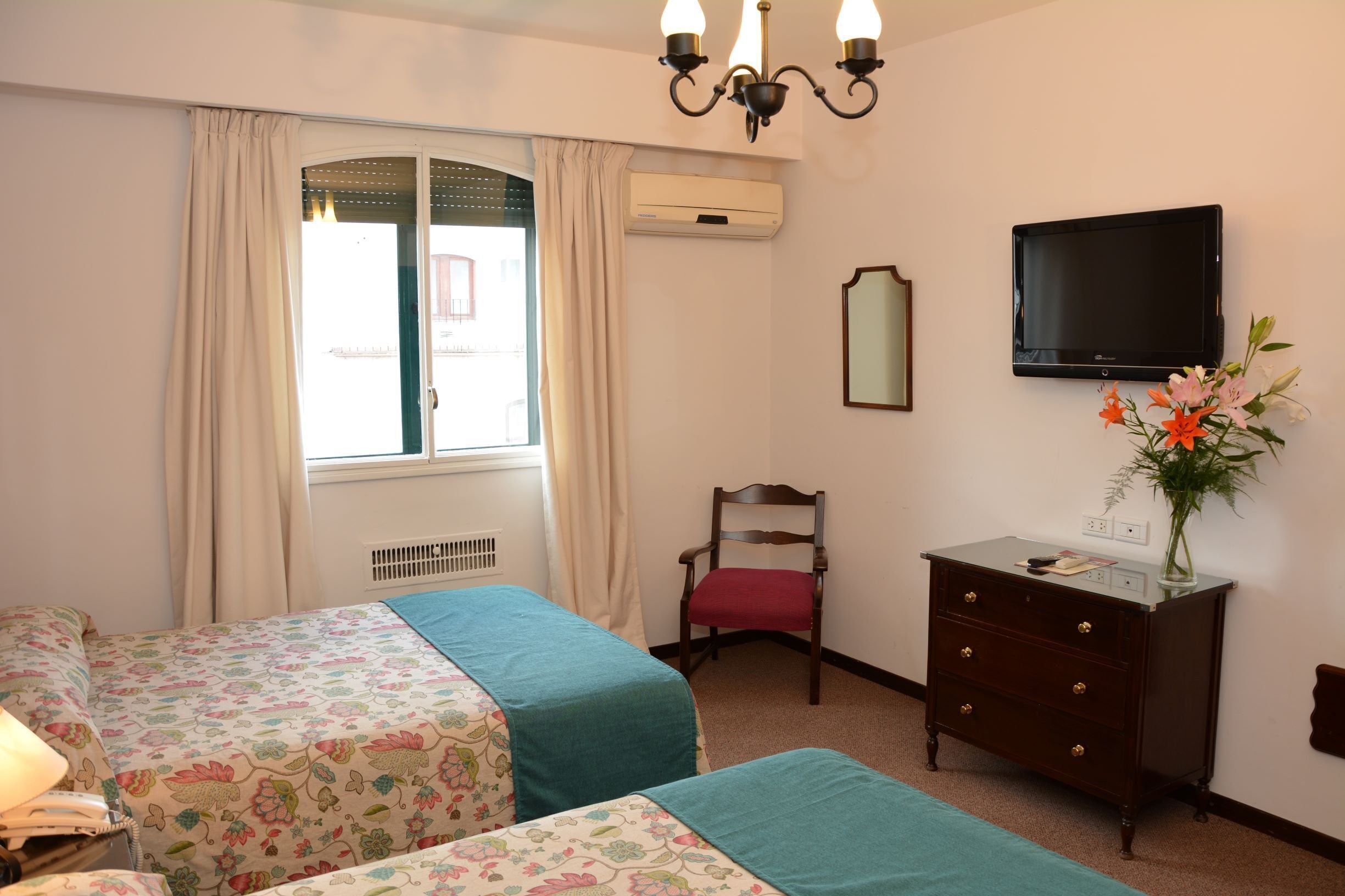 Une chambre d’hôtel avec deux lits, une télévision, une commode, une chaise et une fenêtre avec des rideaux.