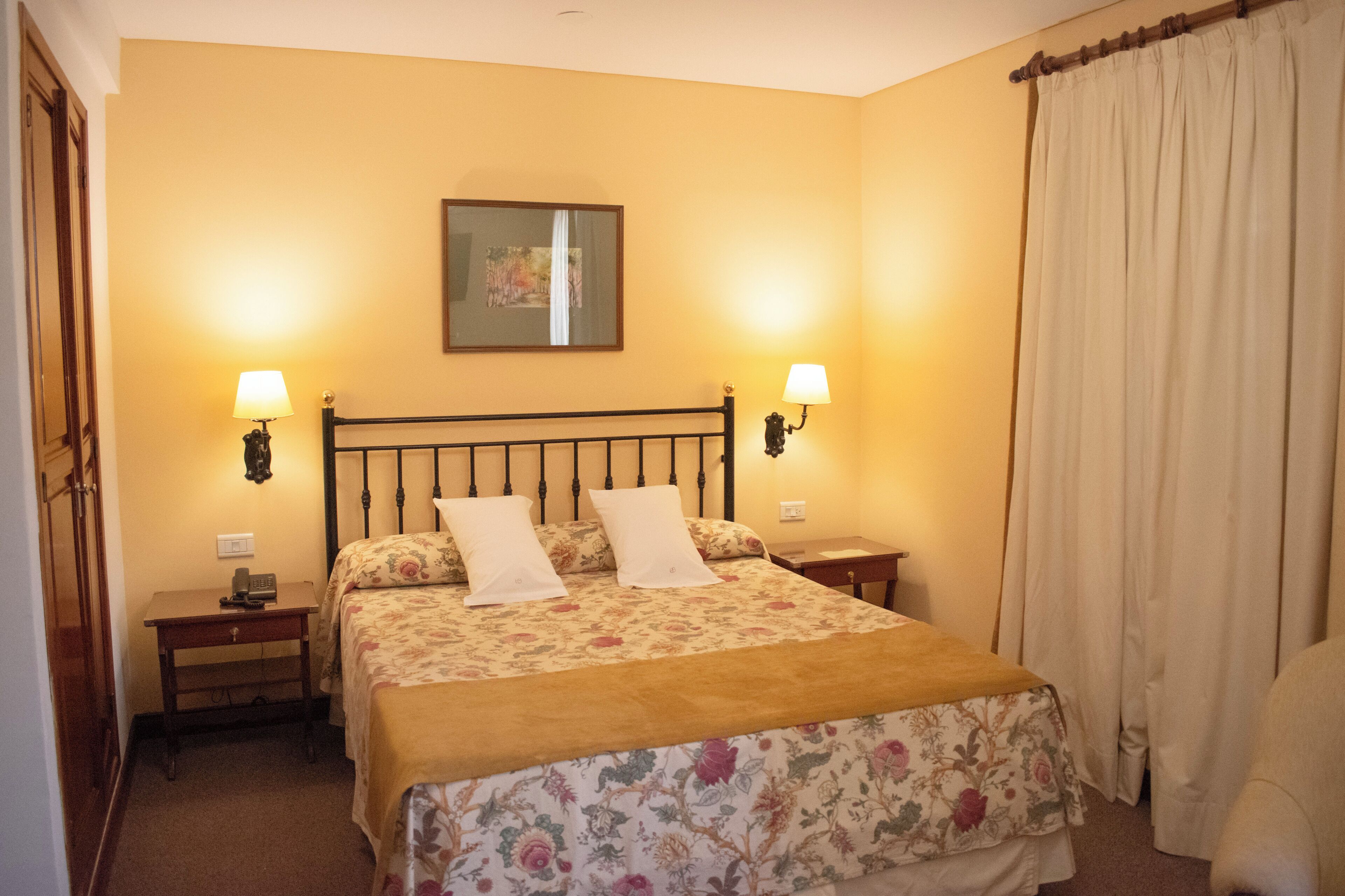 A neatly arranged bedroom with a bed, bedside lamps, a nightstand, and a painting on the wall.