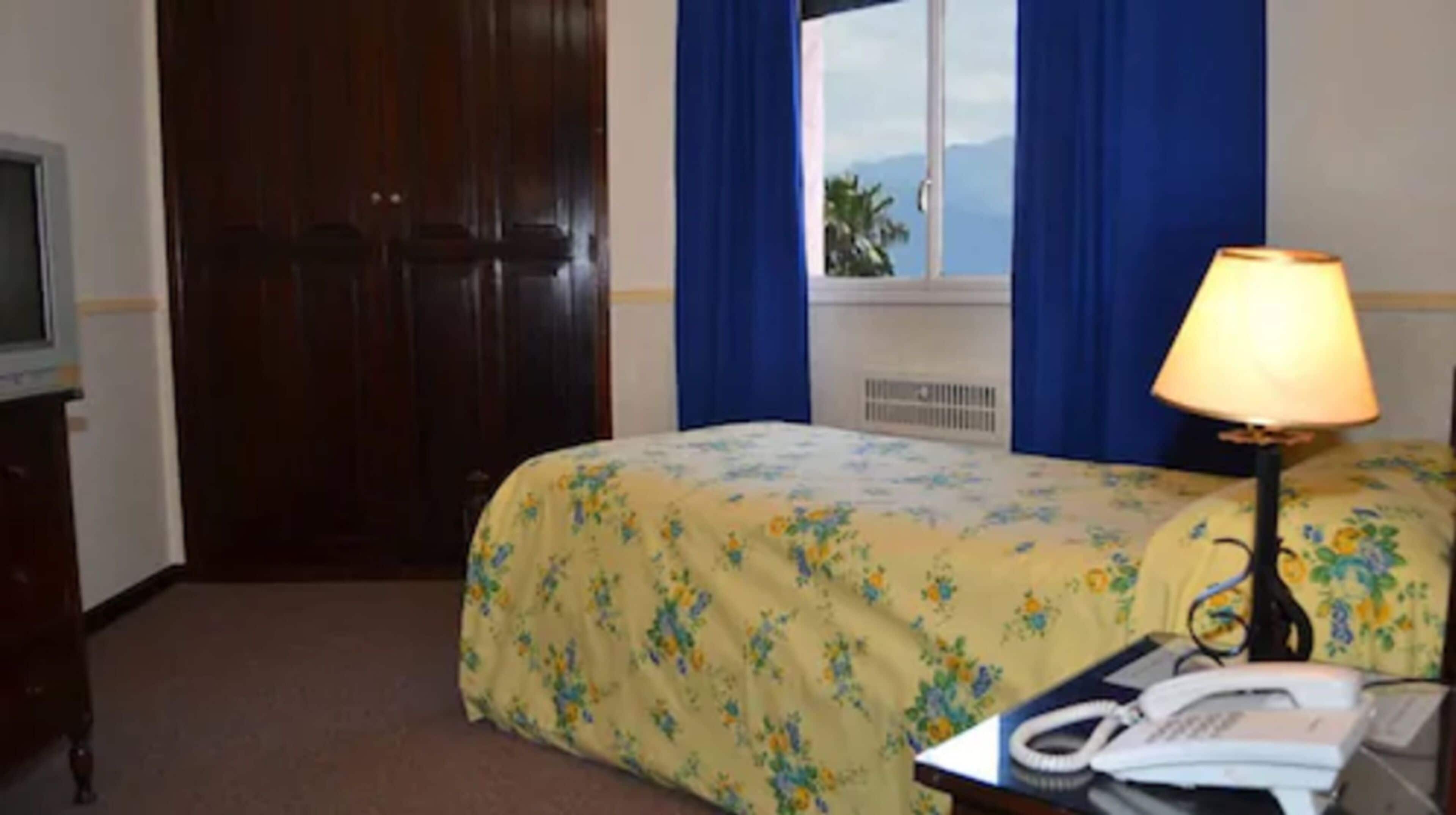 Une chambre d’hôtel avec un lit, un bureau avec un téléphone et une fenêtre avec des rideaux.