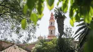 A swimming pool with a tiled deck, surrounded by greenery and a building with a bell tower in the background.