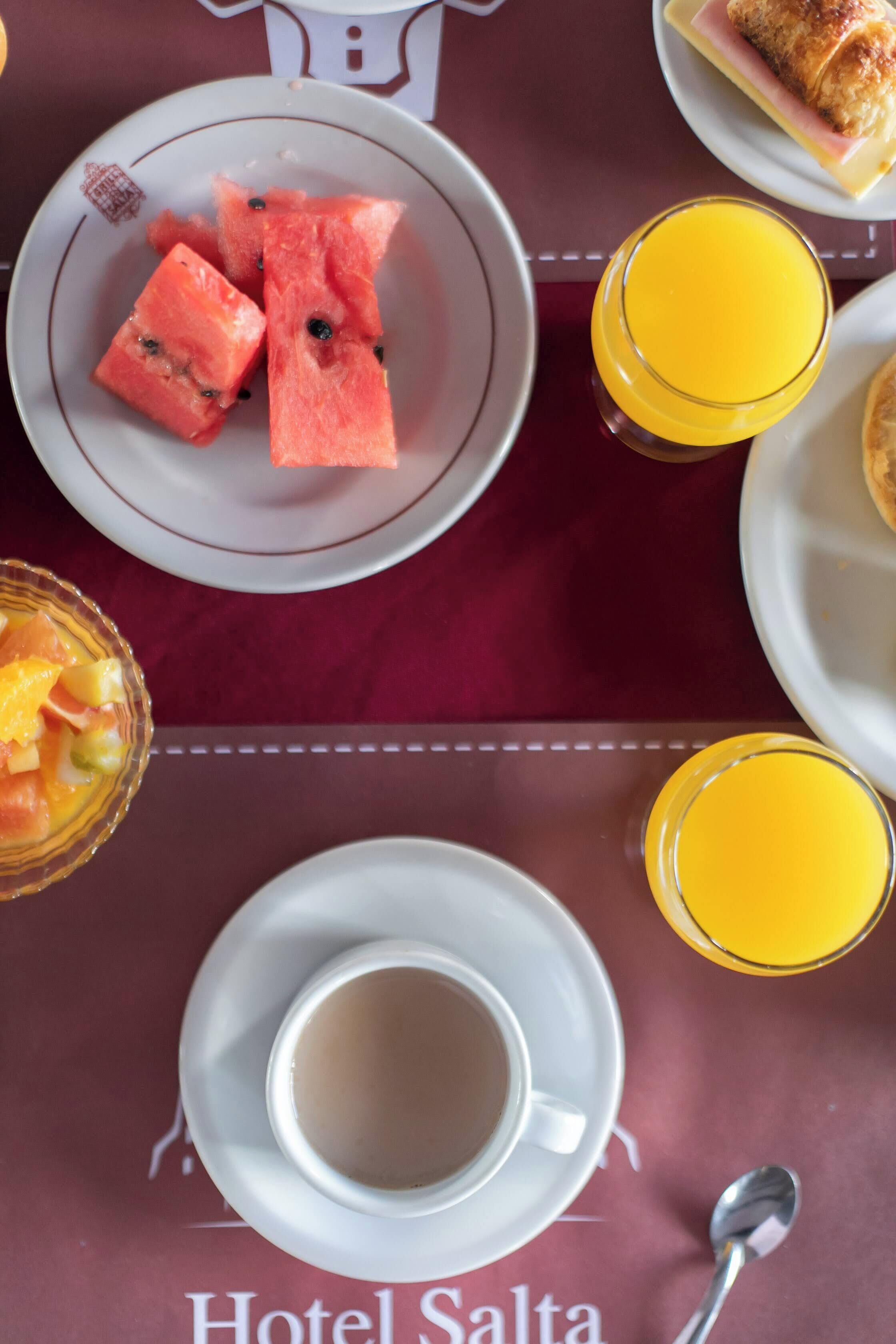 Desayuno con sandía, naranja y una taza de café sobre una mesa.