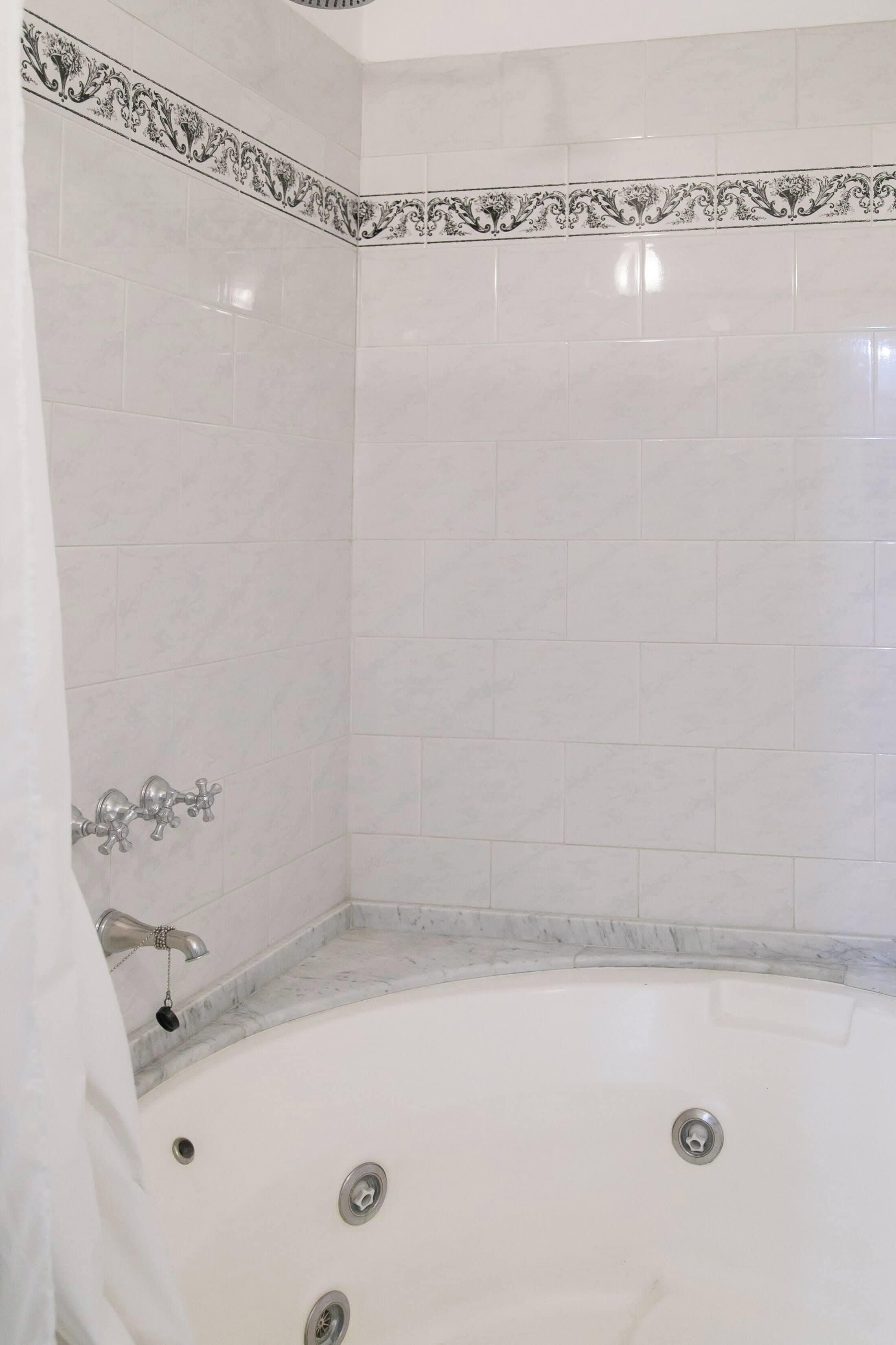 Un baño con bañera, azulejos blancos y un detalle decorativo.