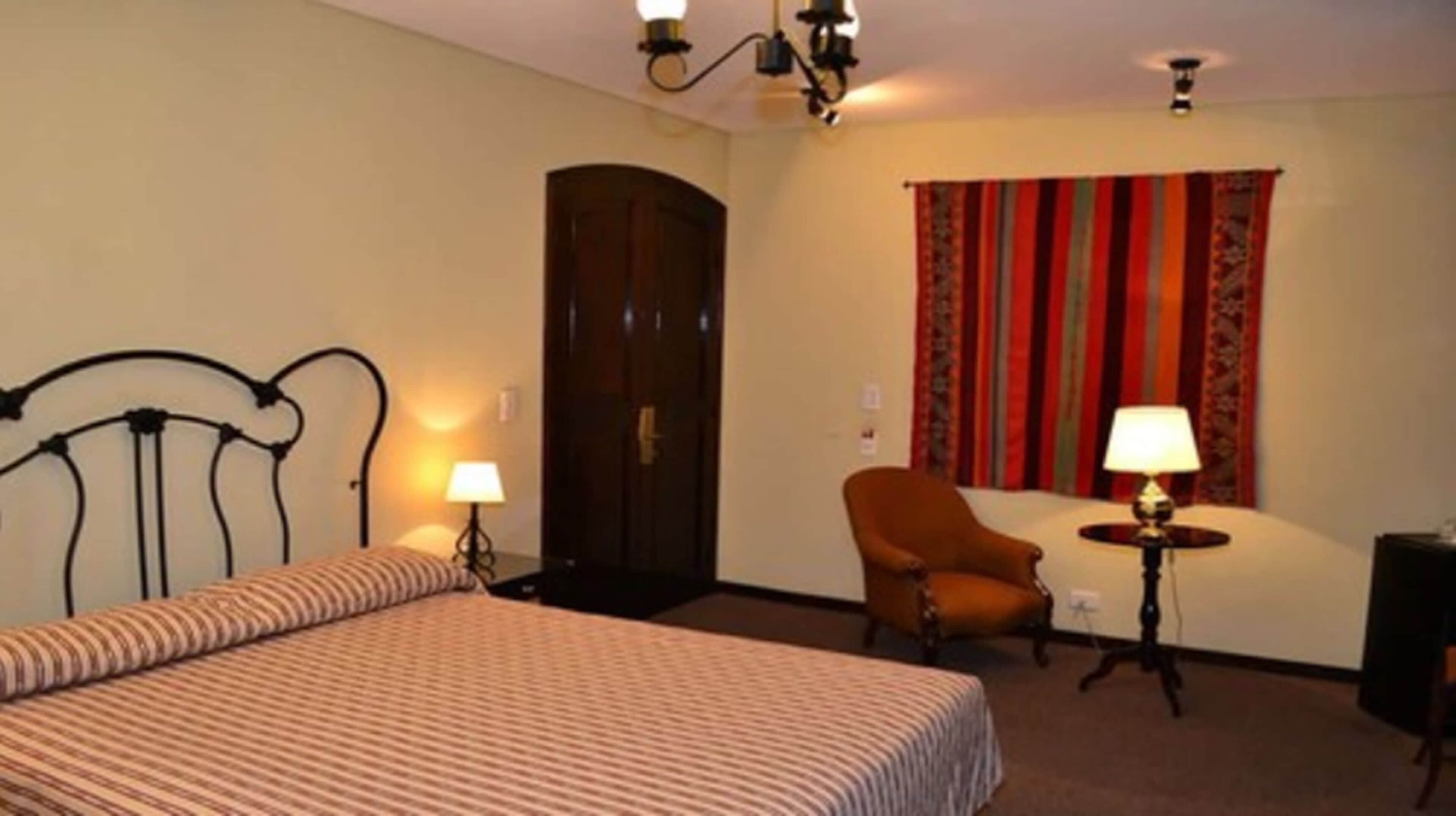 A hotel room with a bed, a chair, a desk, and a lamp.