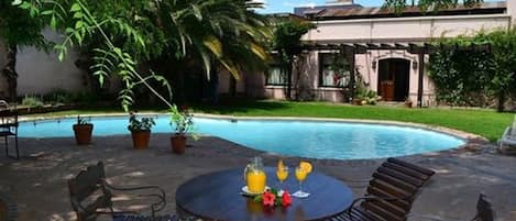 Un área junto a la piscina con una mesa redonda, sillas y plantas en macetas.