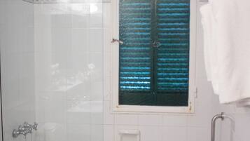 A bathroom with a glass-enclosed shower, a bathtub, a toilet, and a window with blinds.