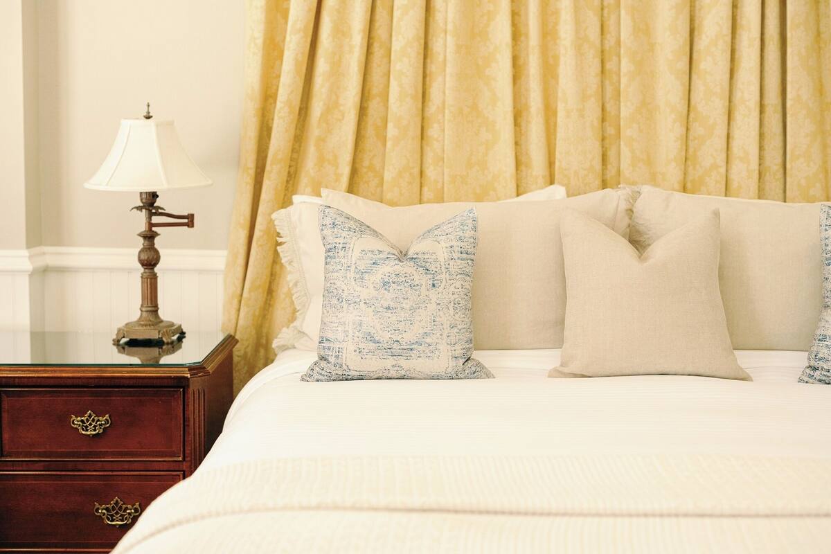 A neatly made bed with patterned pillows, a bedside lamp, and a wooden nightstand with drawers.