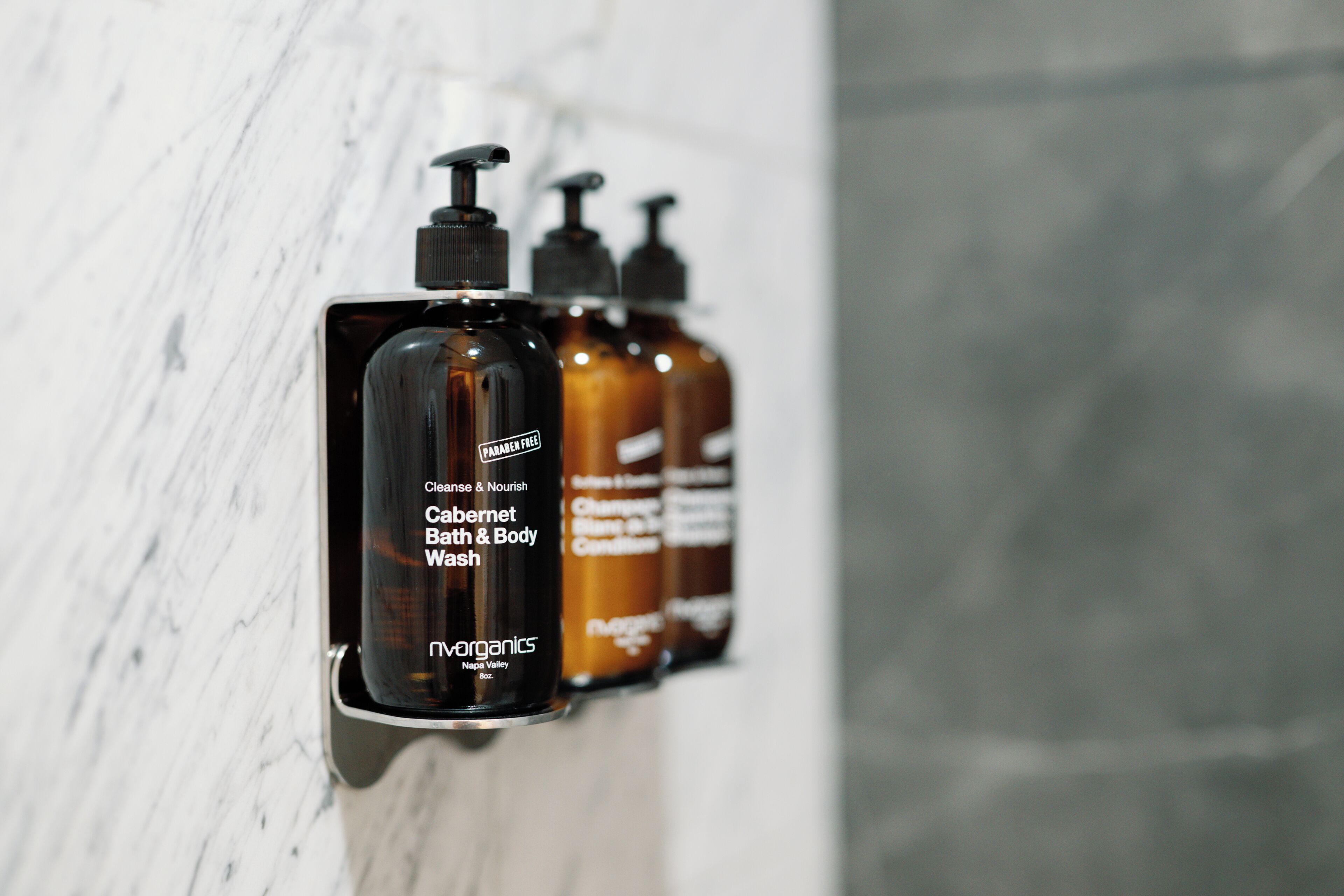 A wall-mounted dispenser with three bottles of bath and body wash.