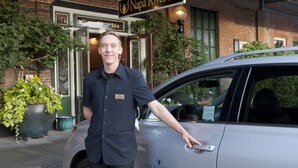 Un homme en uniforme se tient à côté d’une voiture, et l’enseigne du Napa River Inn est visible au-dessus.