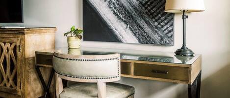 A wooden desk with a chair, a lamp, a potted plant, and a large black and white artwork on the wall.