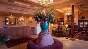 A lobby with a marble reception desk, a large vase with flowers, a chandelier, and a seating area with a patterned ottoman.
