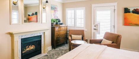 A hotel room with a fireplace, a bed, a chair, a dresser, and artwork on the walls.
