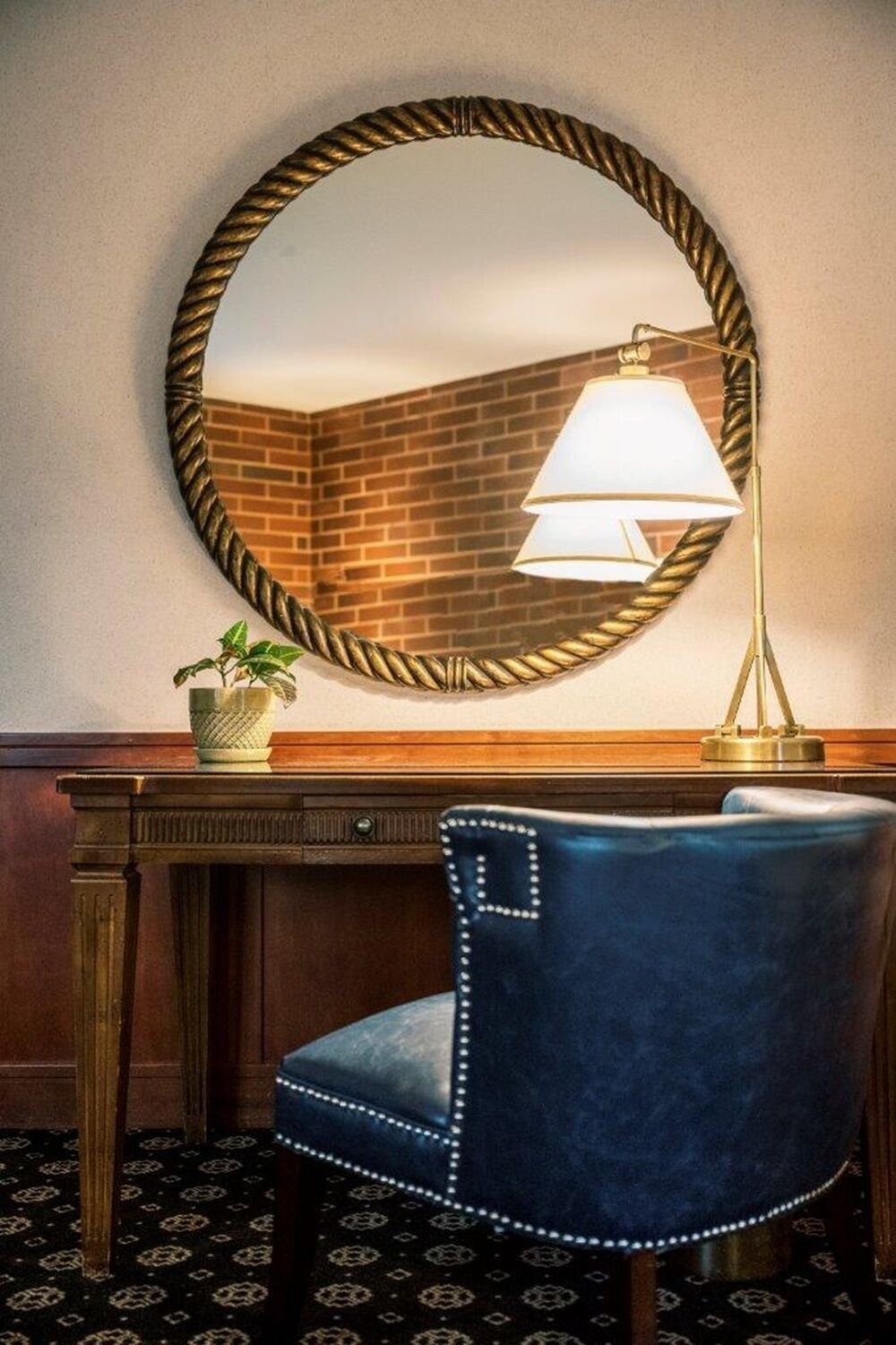 A room with a round mirror, a desk, a chair, and a lamp.