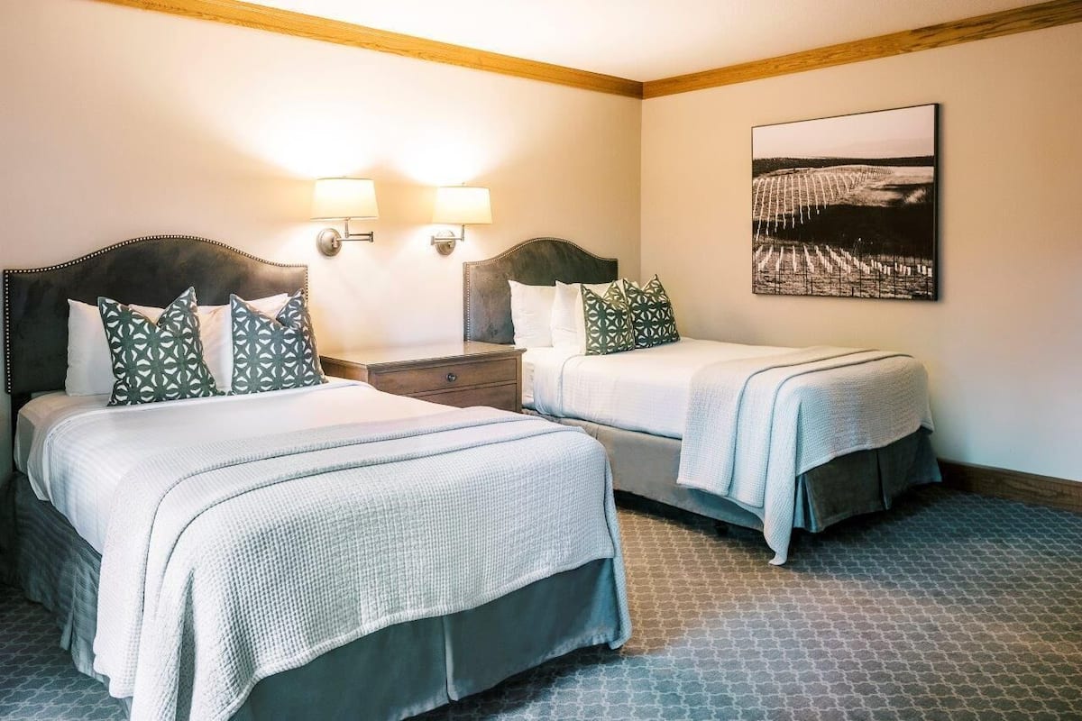 A hotel room with two beds, a nightstand, wall-mounted lamps, and a framed picture.