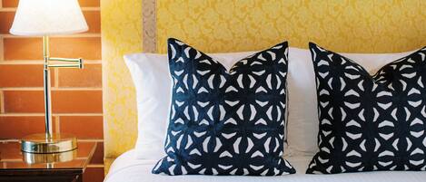 A hotel room with a brick wall, a bed with white bedding, and patterned pillows.