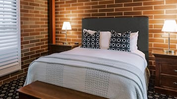 Une chambre d’hôtel avec un mur décoré d’un motif en briques, un grand lit avec une literie à motifs, deux lampes de chevet et un banc en bois.