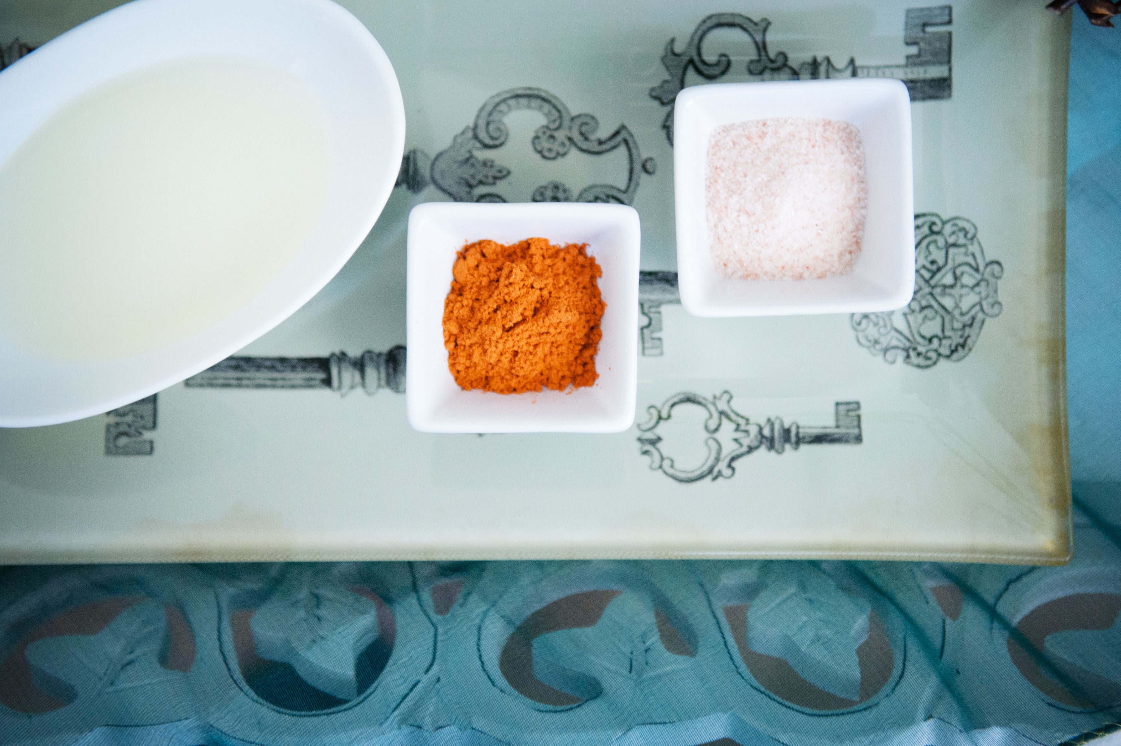A tray with three bowls containing different substances, placed on a table with a patterned design.