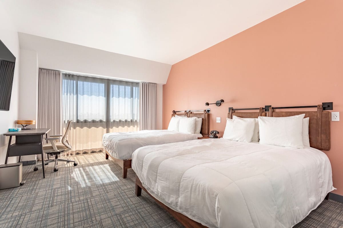 A hotel room with two beds, a desk, and a chair.