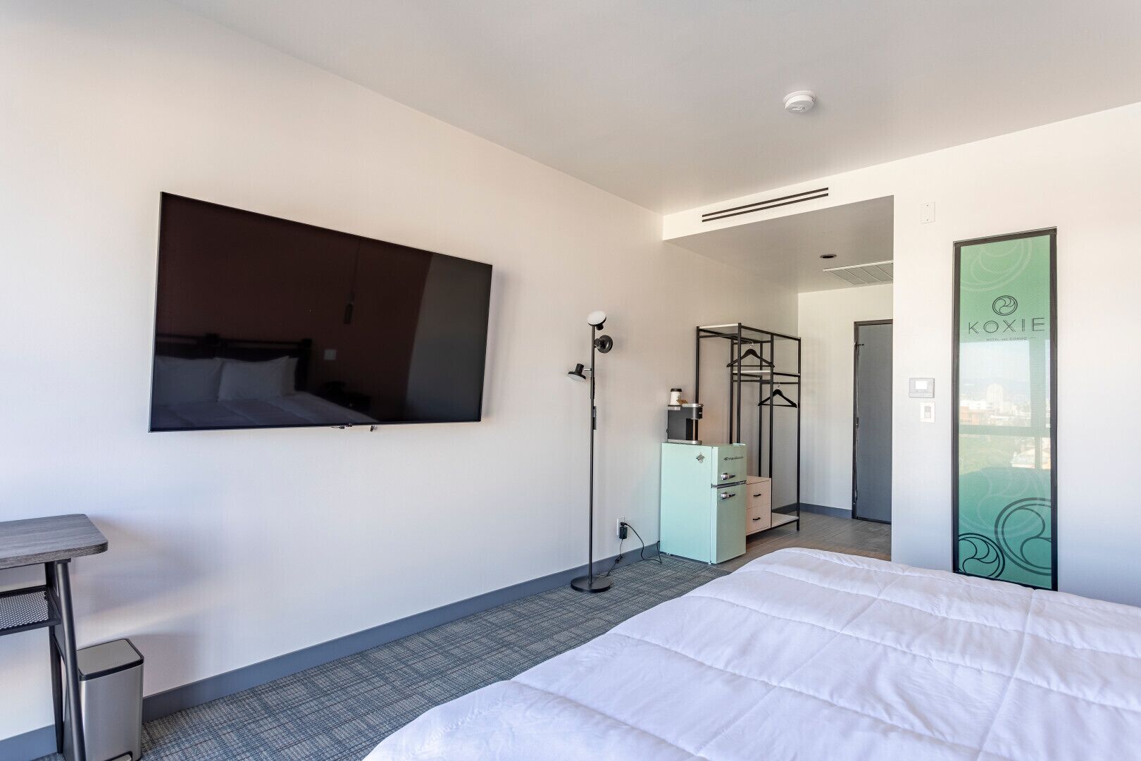 A hotel room with a bed, a desk, a wardrobe, a mirror, and a TV mounted on the wall.