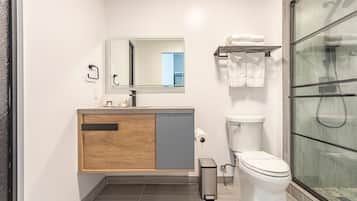 A modern bathroom with a wooden vanity, a toilet, and a glass shower enclosure.
