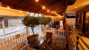 An outdoor seating area with tables and chairs, a potted tree, and a coin laundry service in the background. - Hotel Koxie (Los Angeles)