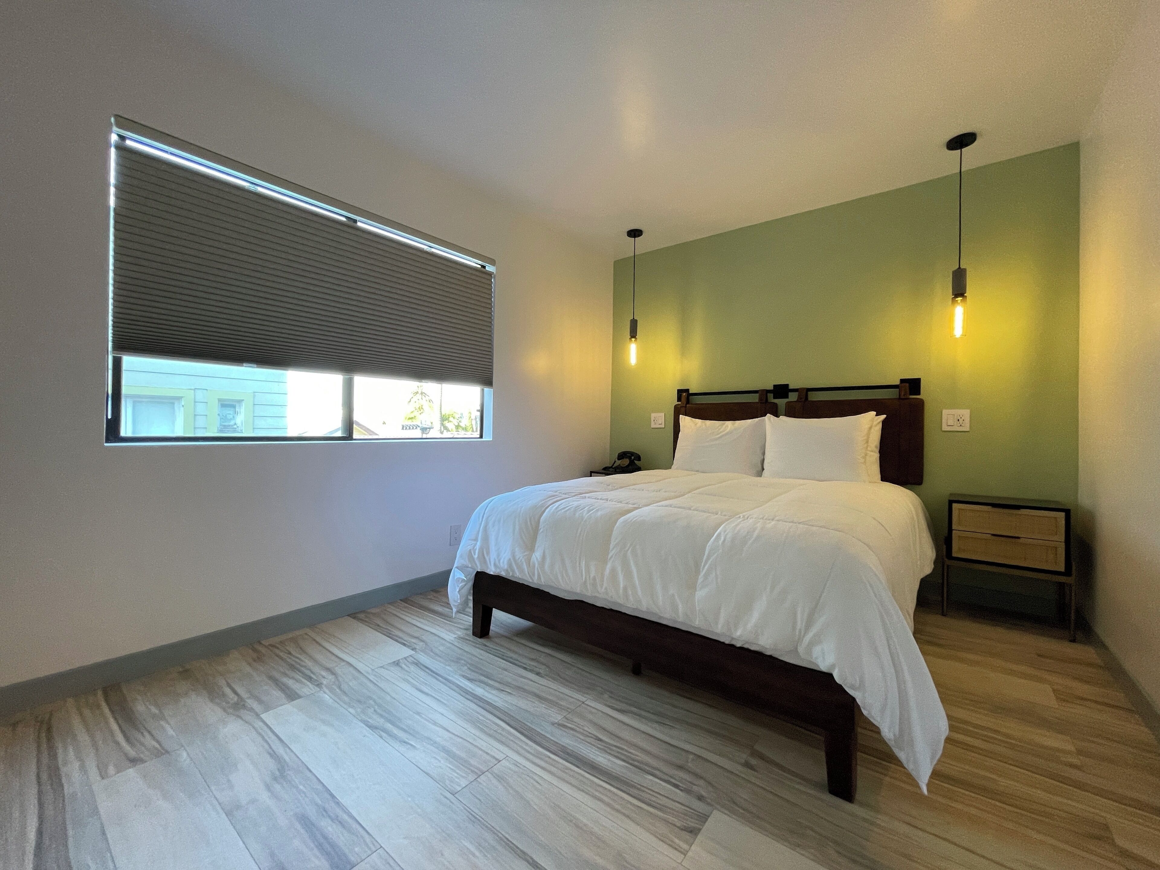 A bedroom with a bed, a nightstand, a lamp, and a window with blinds.