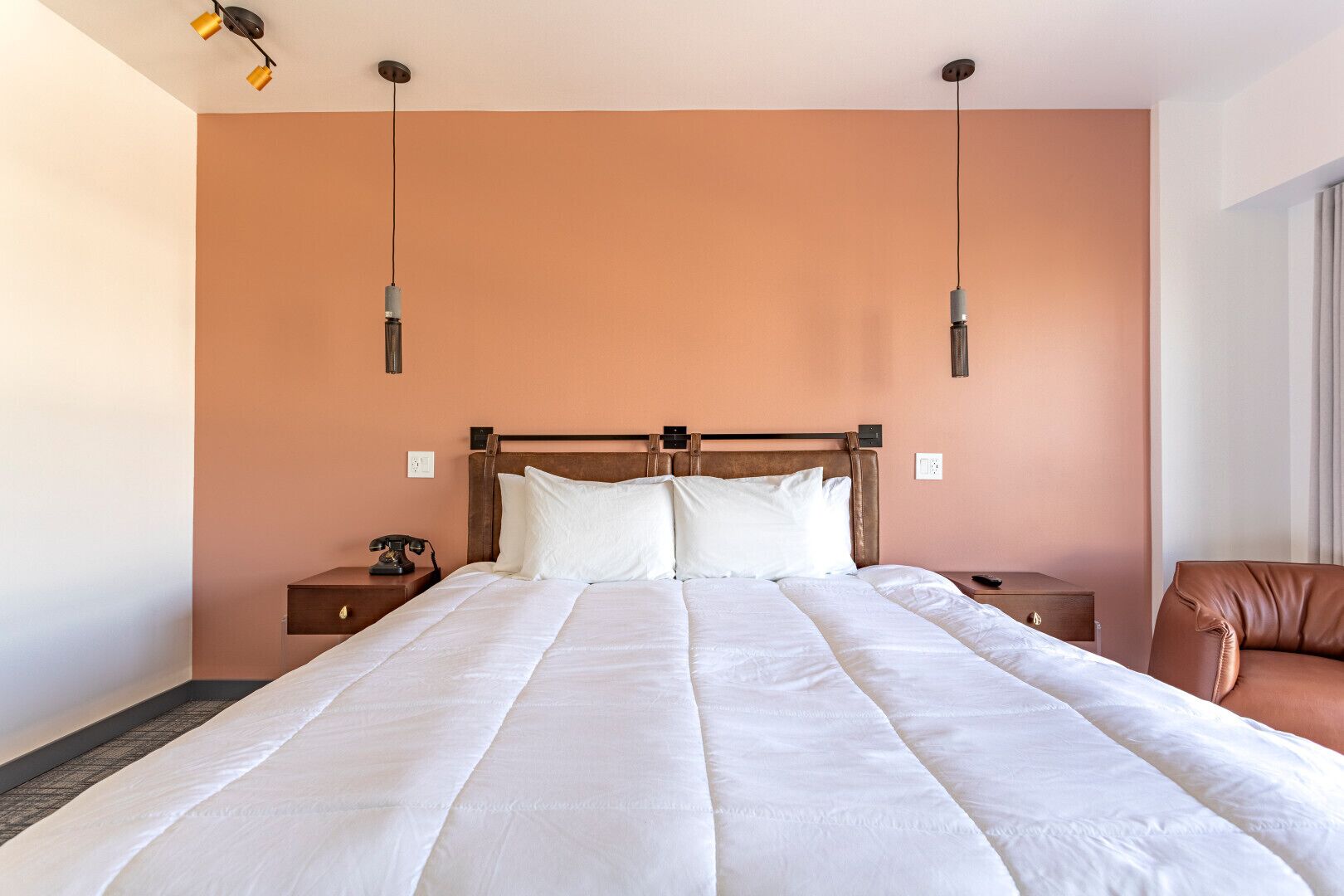 A large bed with a wooden headboard, two bedside tables, and a brown leather chair.