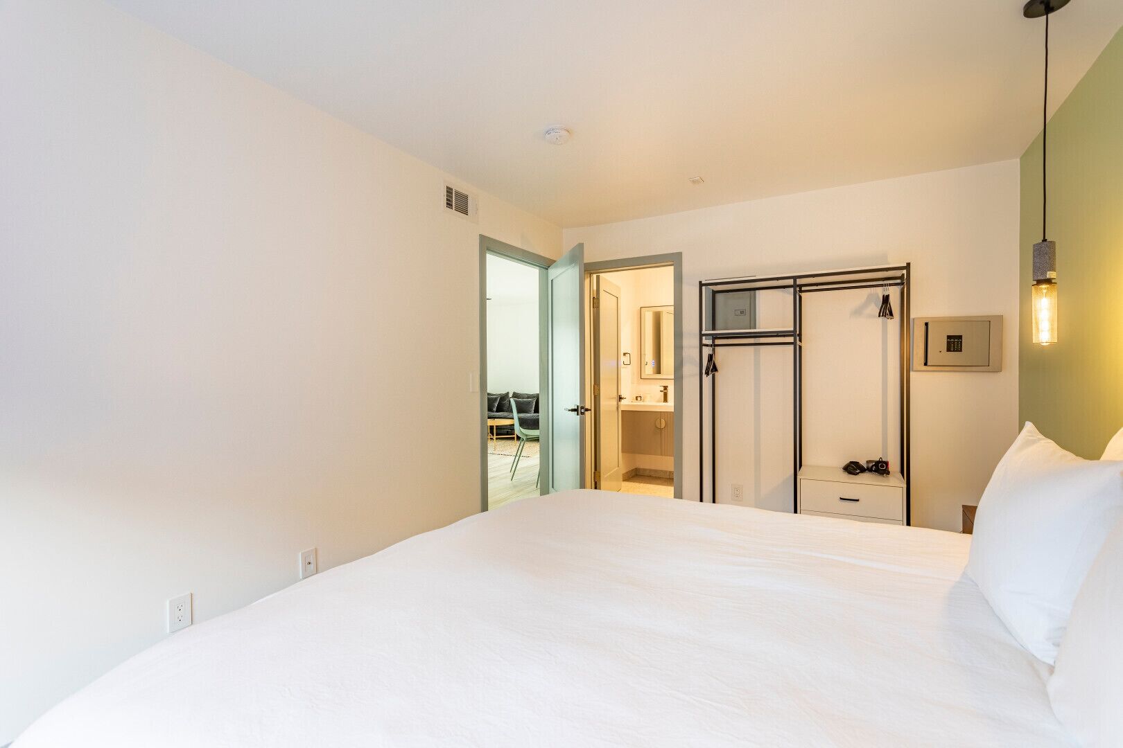Une chambre d’hôtel avec un grand lit, une armoire, un miroir et un luminaire suspendu.