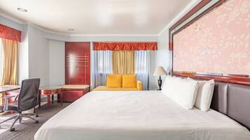 A hotel room with a large bed, a desk, a chair, and a sofa.
