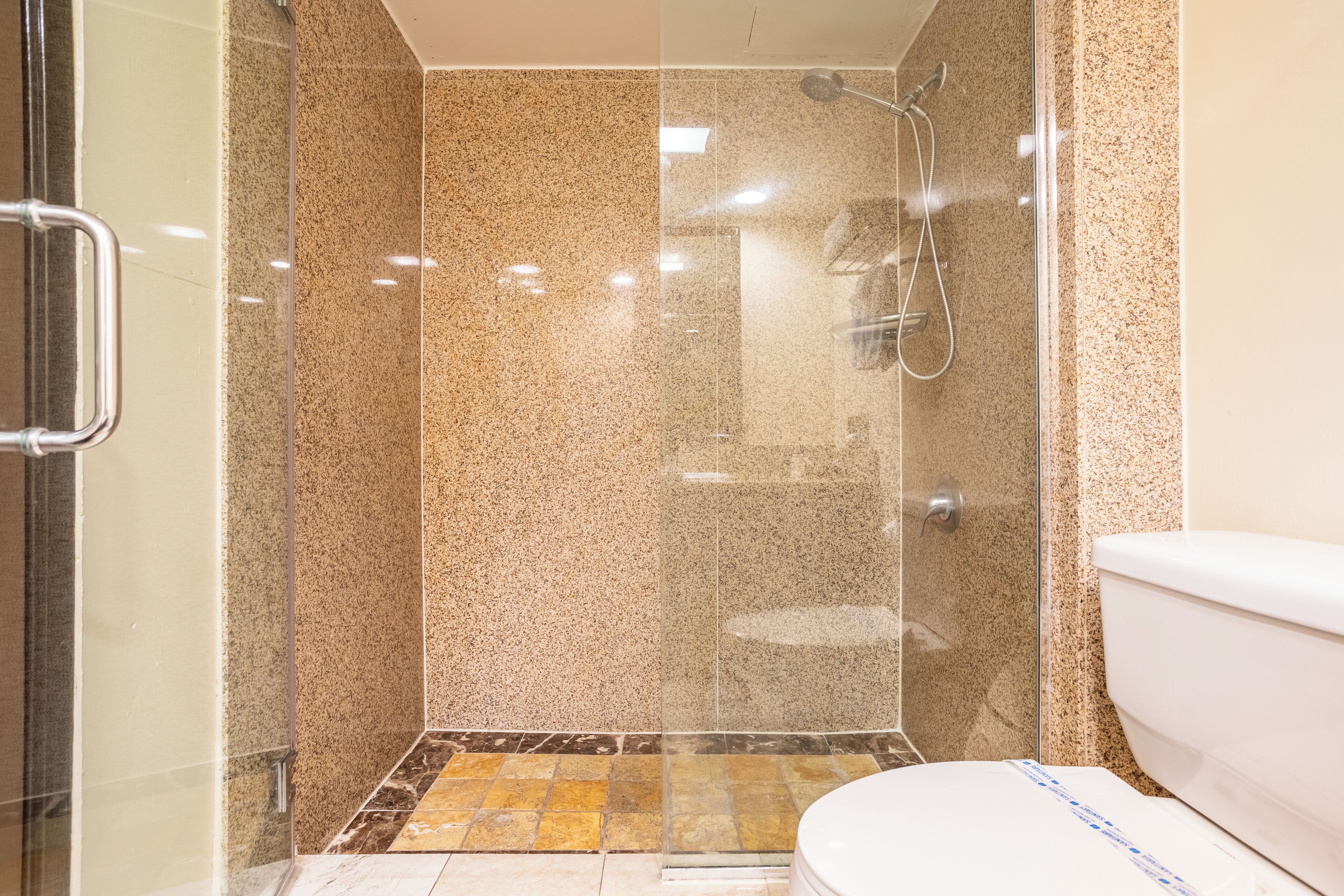 A modern bathroom with a glass-enclosed shower, a toilet, and a tiled floor.