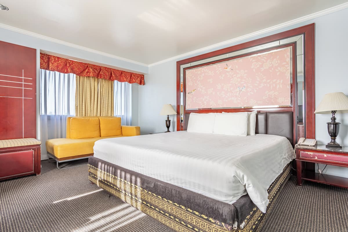 A hotel room with a large bed, a sofa, a desk with a lamp, and a mirror.