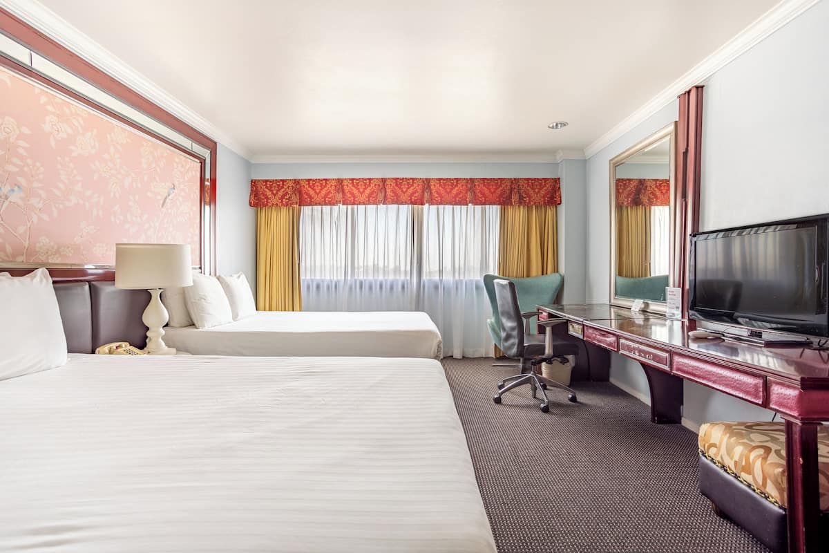 A hotel room with two beds, a desk with a television, a chair, and a large mirror.