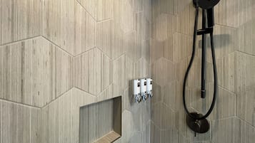 Un área de ducha con un diseño de baldosas hexagonales, un estante integrado y un cabezal de ducha de mano.