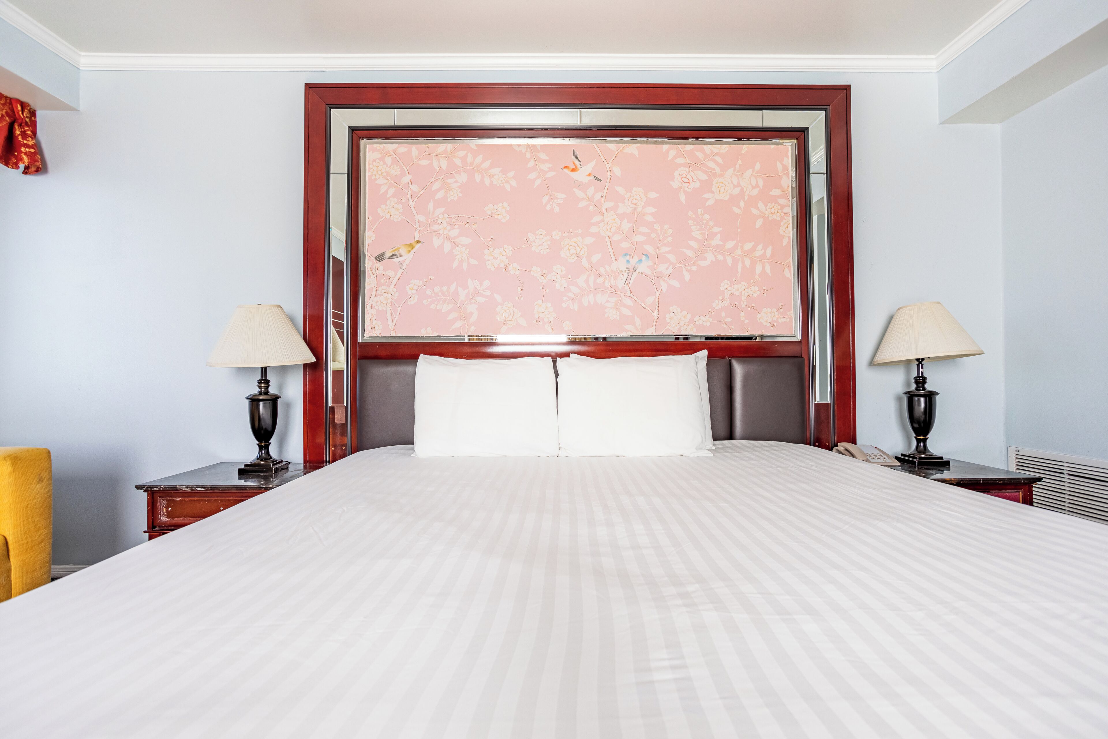 Ein Hotelzimmer mit einem großen Bett, zwei Nachttischen mit Lampen, einem Spiegel über dem Bett und floralem Wandpapier.