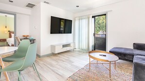 A modern living room with a flat-screen TV, a sofa, a dining area with chairs, and a large window with curtains. - Hotel Koxie (Los Angeles)