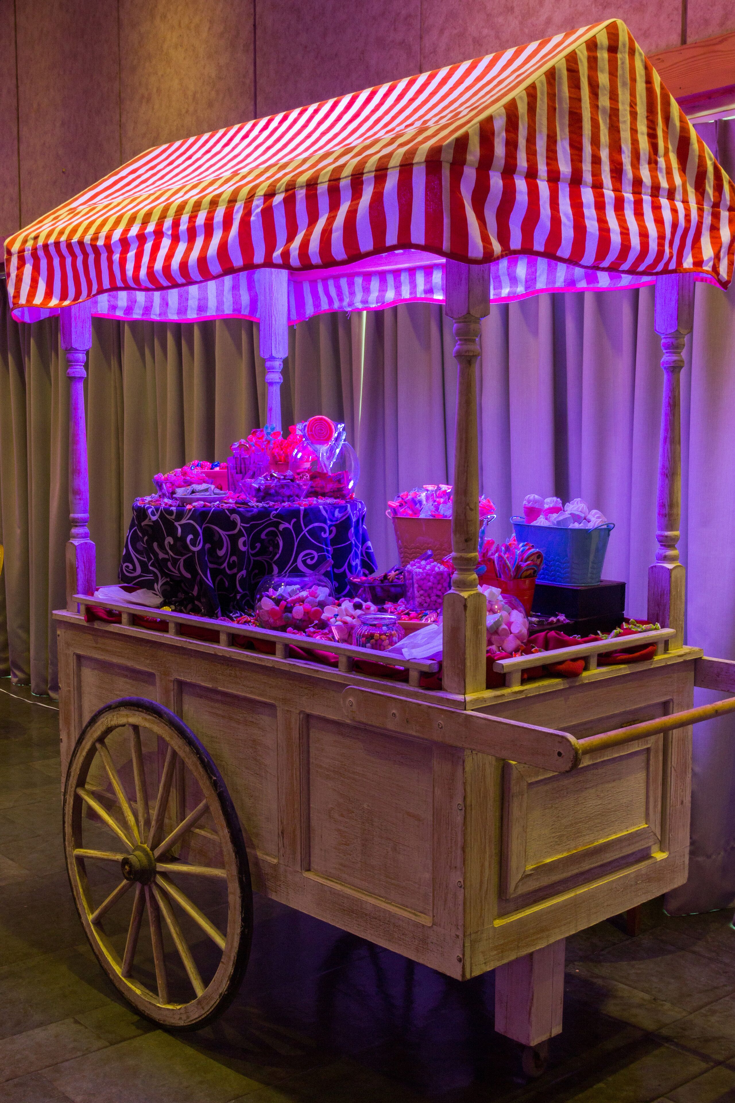 A vintage-style cart with a striped canopy, filled with various items and illuminated by purple lighting.