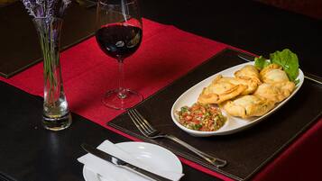 A table set with a red placemat, a white plate with pastries, a glass of red wine, and a vase with flowers.