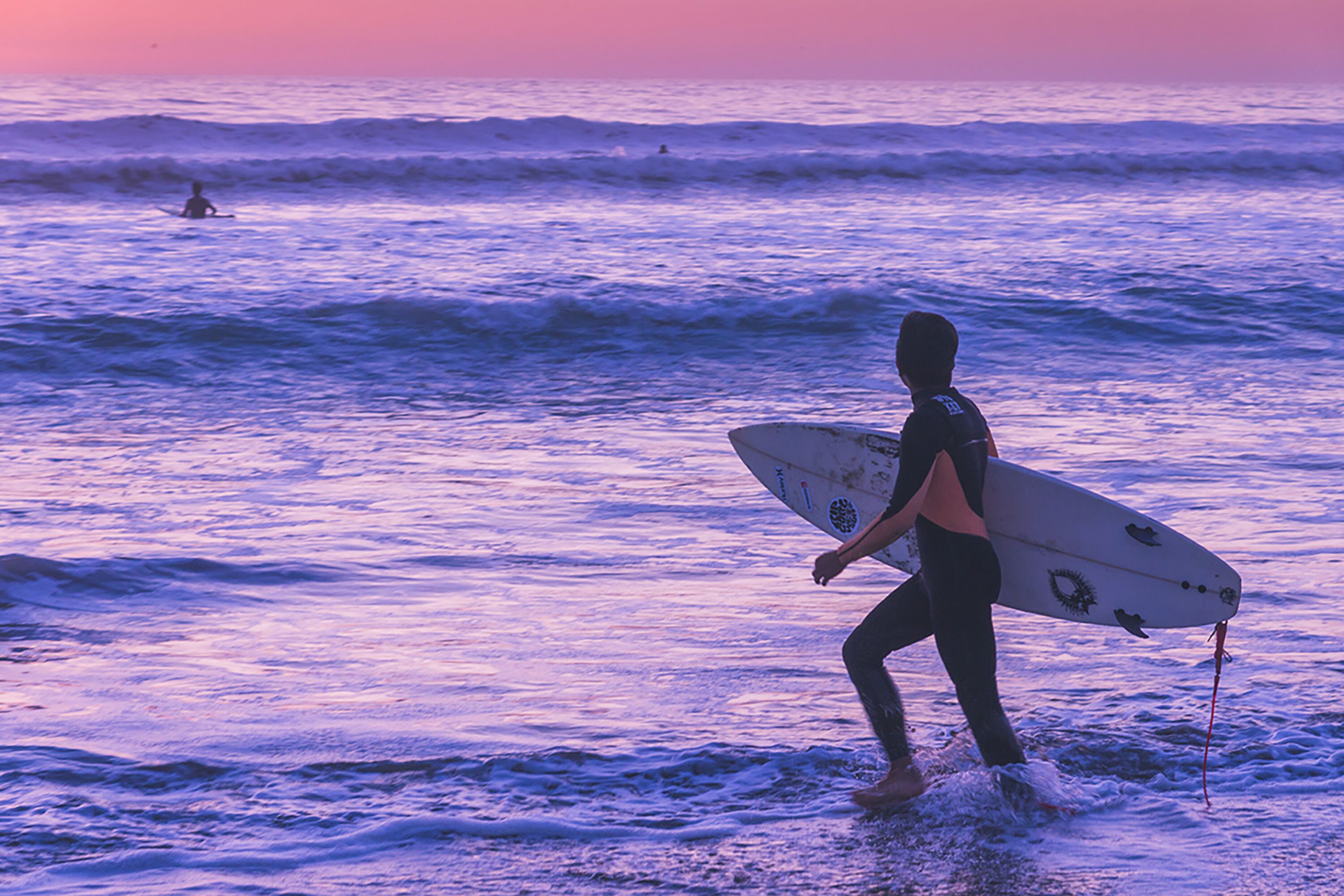 A person carrying a surfboard walking through the water.