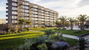 Un hotel moderno de varios pisos con un patio que cuenta con palmeras, una fuente y mobiliario exterior.