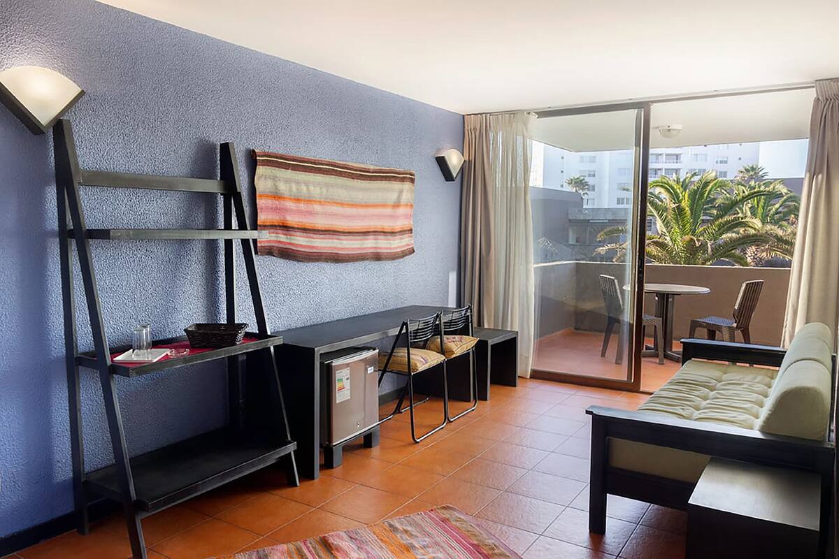 Une chambre d’hôtel compacte dotée d’un balcon, d’un canapé, d’une petite table et d’un bureau avec une chaise.