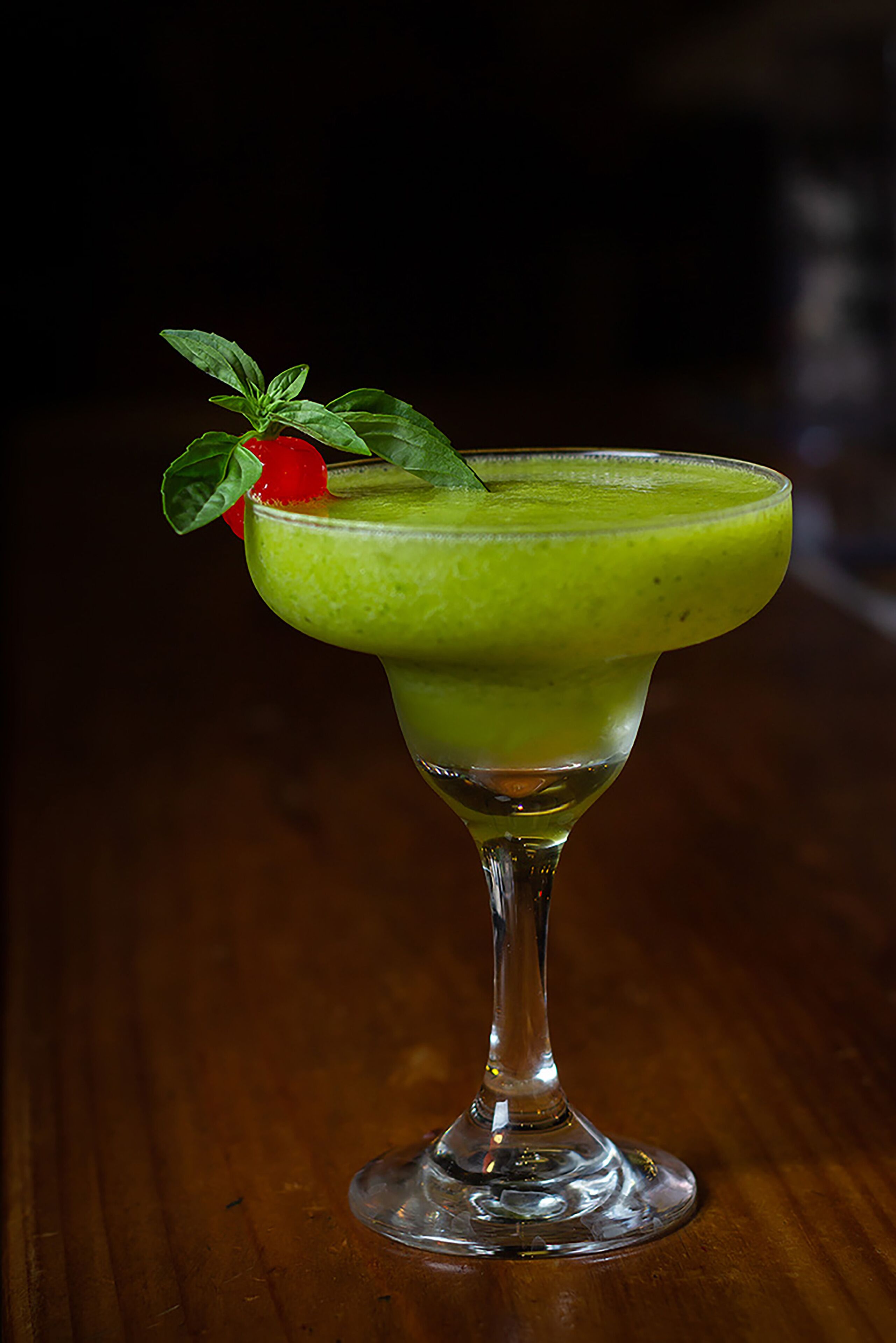 A green cocktail in a martini glass with a strawberry garnish on a wooden surface.