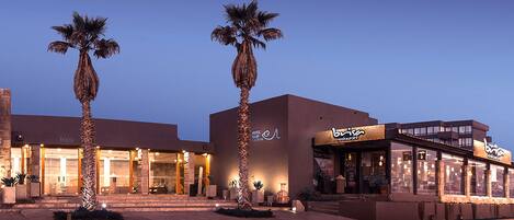 A hotel with a modern facade, palm trees in front, and a restaurant named 'Brisen' on the right.